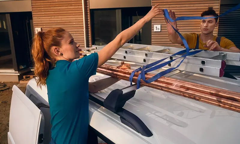 Der Volkswagen Caddy Cargo - Handwerkerin befestigt Arbeitsmaterial auf dem Dach - Jetzt deinen Volkswagen bei deinem Volkswagen Autohaus Mothor in Brandenburg leasen oder finanzieren oder kaufen